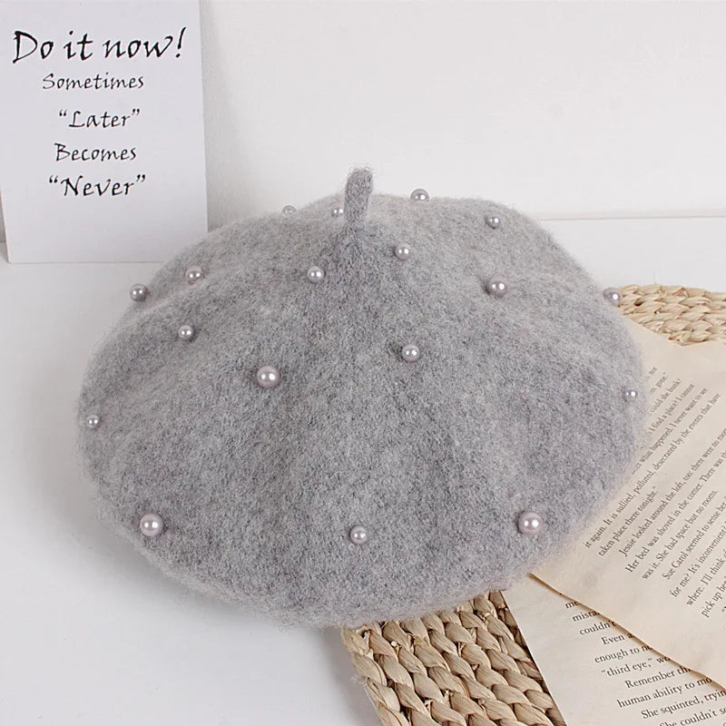Gray beret with pearl embellishments on a textured surface with motivational text.