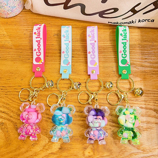 Four colorful keychains with bear charms on a wooden surface, featuring 'Good luck' text.