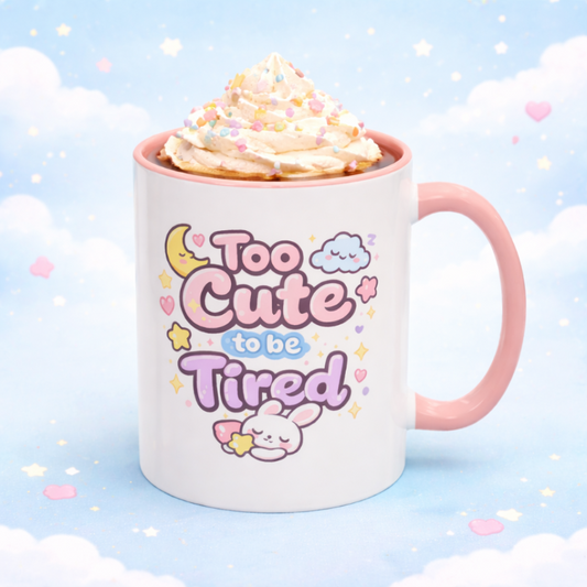 Mug with 'Too Cute to be Tired' text and pink handle on a light blue background
