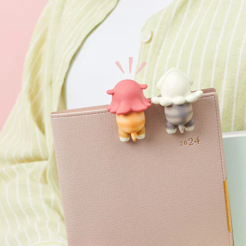 Collage of a notebook with a small robot figurine and a person wearing headphones with a charm, on a pink background.