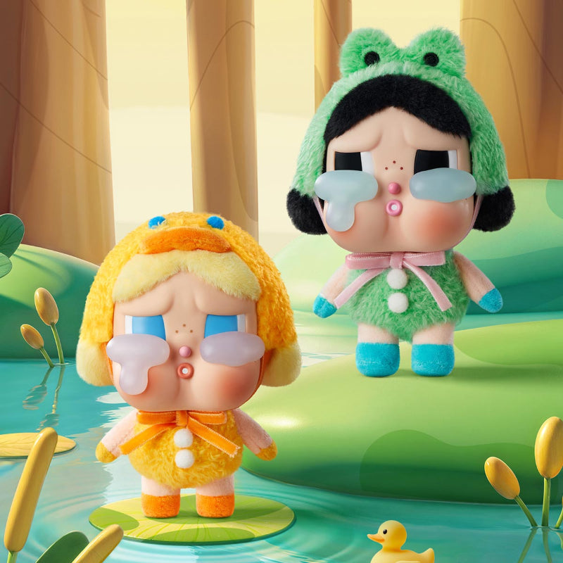 Crybaby kawaii blind box figures, one in a yellow outfit and the other in a green frog costume, standing on lily pads with a duck and water plants in the background.