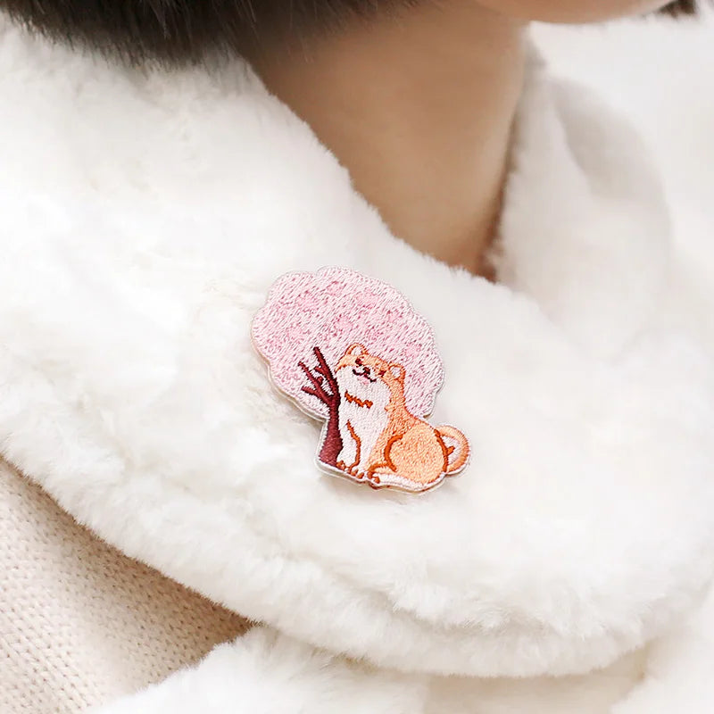Kawaii Cherry Blossom Iron-On Embroidery Patches , this patch is being displayed on a white fluffy scarf, the design used is the shiba inu sat next to the cherry blossom tree.