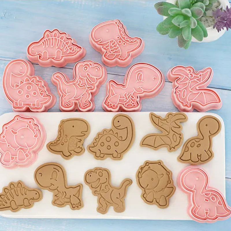 Dinosaur-shaped cookie cutters on a blue wooden surface with a small plant in the corner.
