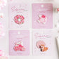 Kawaii Cherry Blossom Iron-On Embroidery Patches come in  four different designs , one with a shiba inu sat next to a cherry blossom tree, another with a white bird flying with a cherry blossom flowers positioned on its wings, also a cat waving and a row of cherry blossom flowers in front , and the last one is the cherry blossoms in a wreath formation. they are all individually in their kawaii packaging on a white background