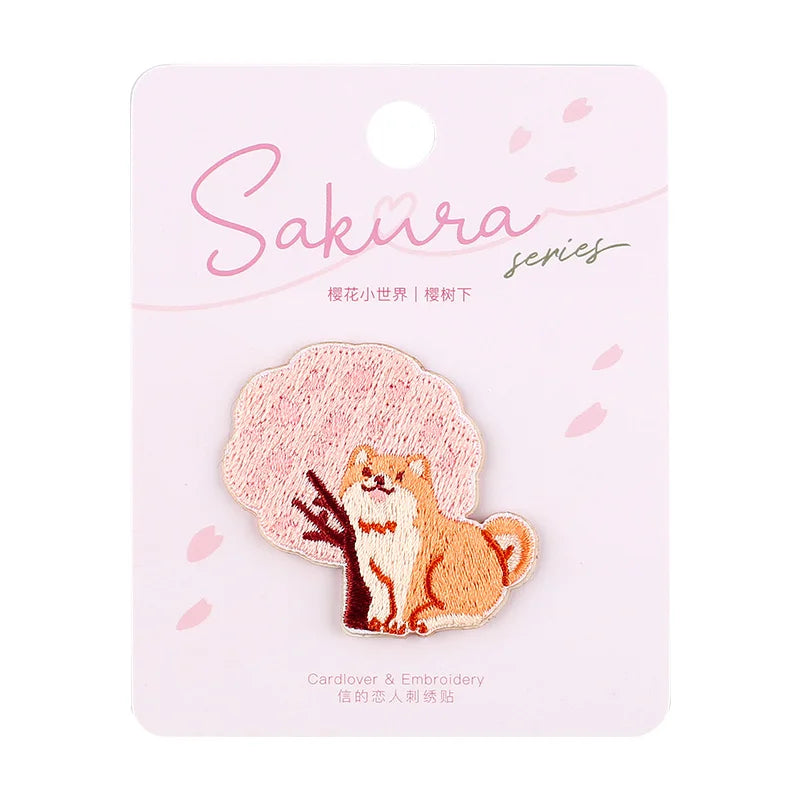 Kawaii Cherry Blossom Iron-On Embroidery Patch is being displayed in its kawaii packaging but this is the shiba inu version sat next to cherry blossom