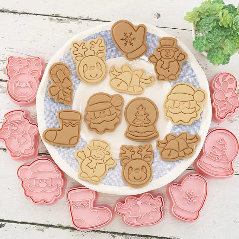 Set of Christmas-themed cookie cutters with baked cookies on a white plate.