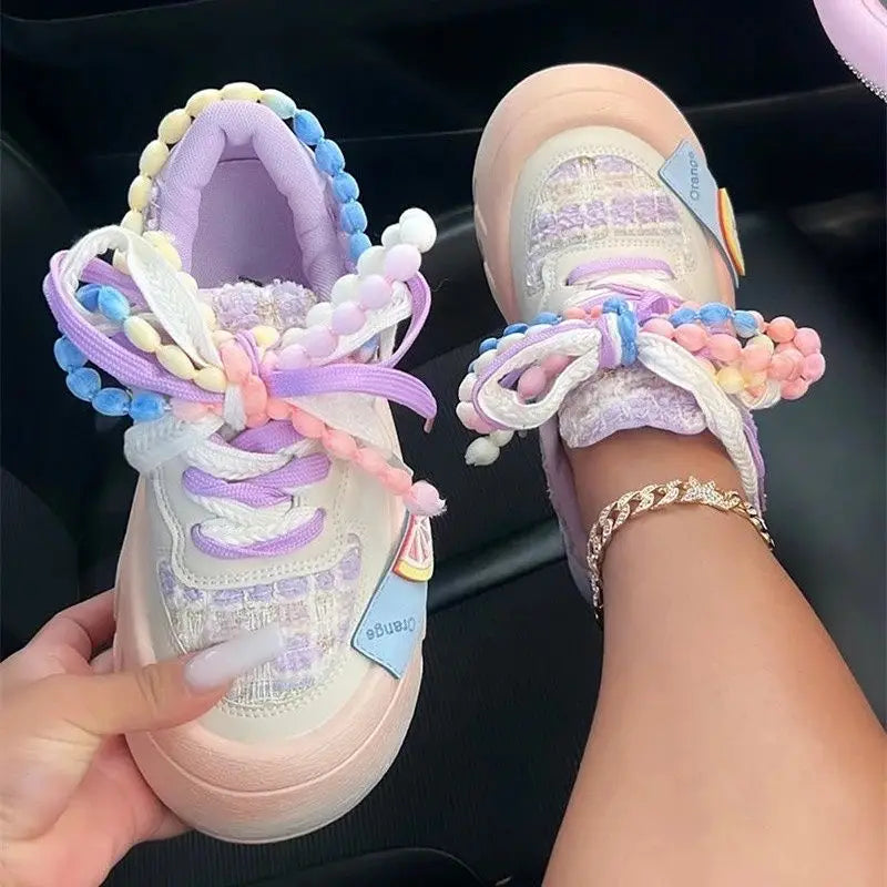 Kawaii Pastel-colored sneakers with decorative pearl 
laces held by a hand.