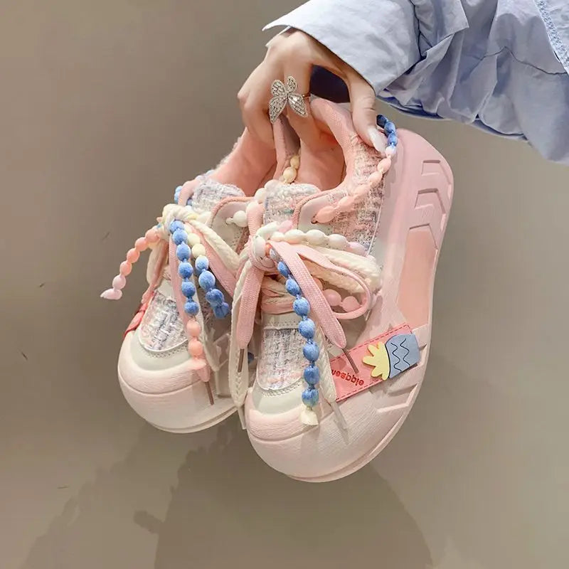 Kawaii Pastel-colored sneakers with decorative pearl elements held by a hand against a neutral background