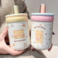 Two cute bear-themed cups held by a person, one with a yellow lid and the other with a pink lid.