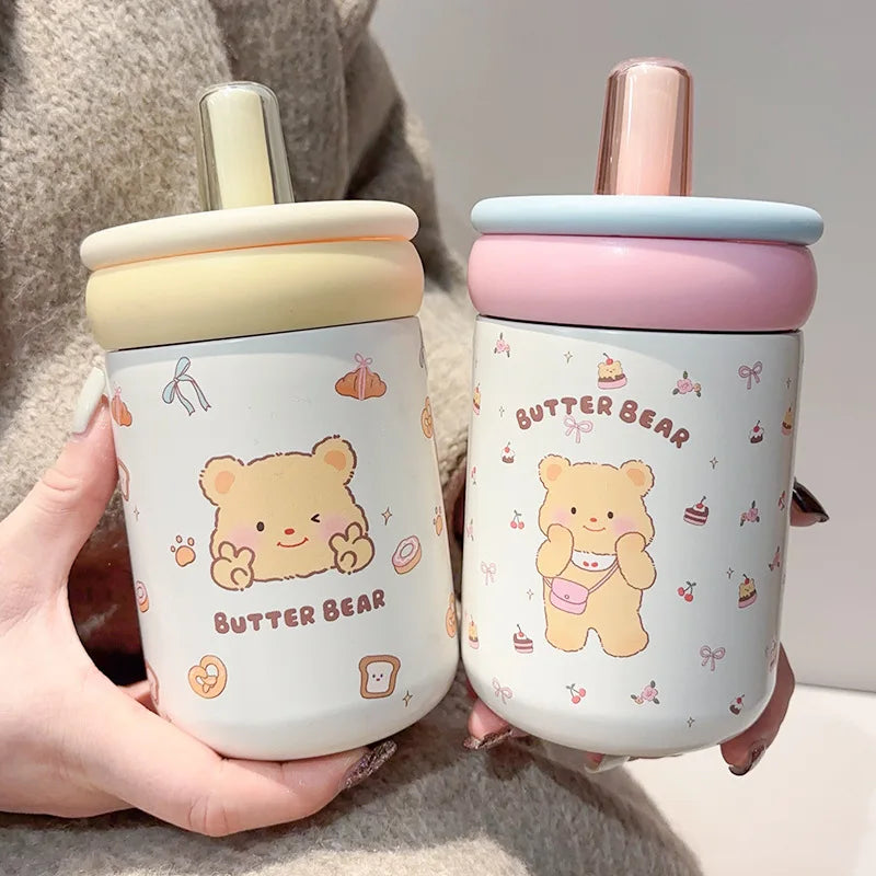 Two cute bear-themed cups held by a person, one with a yellow lid and the other with a pink lid.