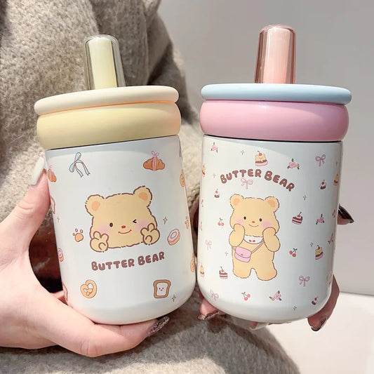 Two cute bear-themed cups held by a person, one with a yellow lid and the other with a pink lid.