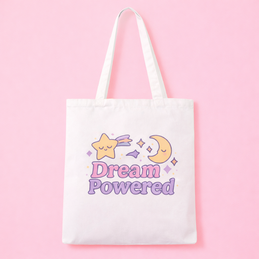 White tote bag with 'Dream Powered' text and shooting star and moon design on a pink background