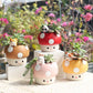 Set of four mushroom-shaped planters with cute animal figurines on a blurred floral background