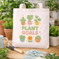 Tote bag with 'Plant Goals' design surrounded by gardening tools and plants