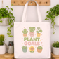 Tote bag with 'Plant Goals' design hanging on a wooden hook with plants in the background.