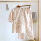 Floral-patterned pajama set hanging on a wooden rack against a white wall.