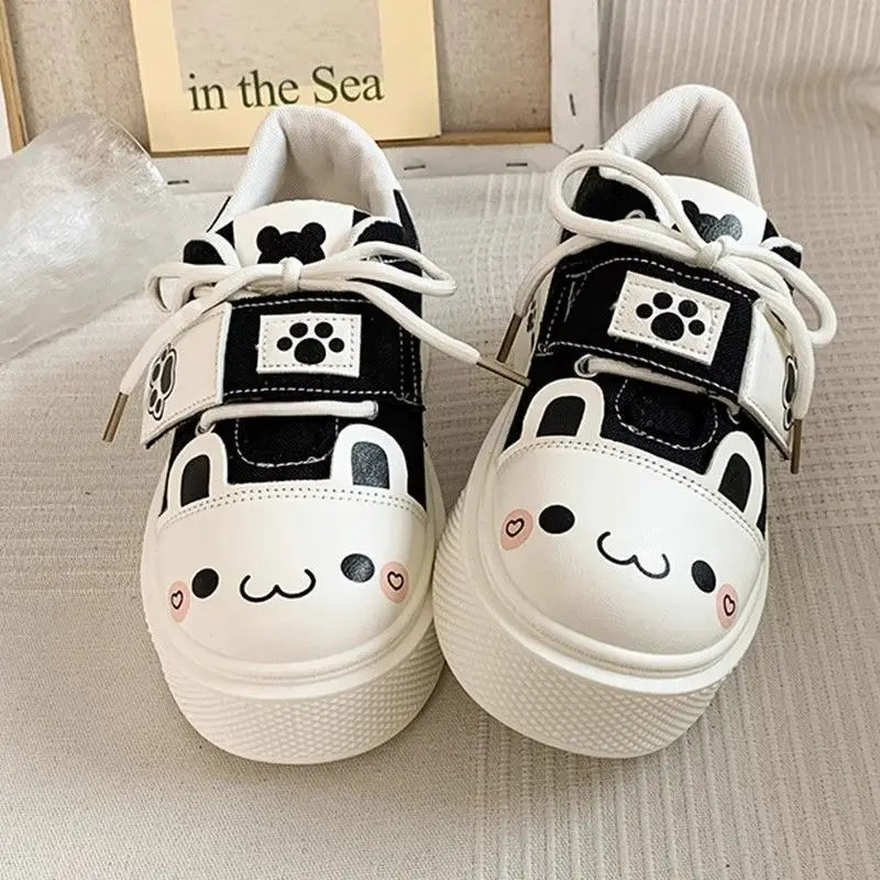 Pair of cute neko white sneakers with black accents and cute face designs on a neutral background