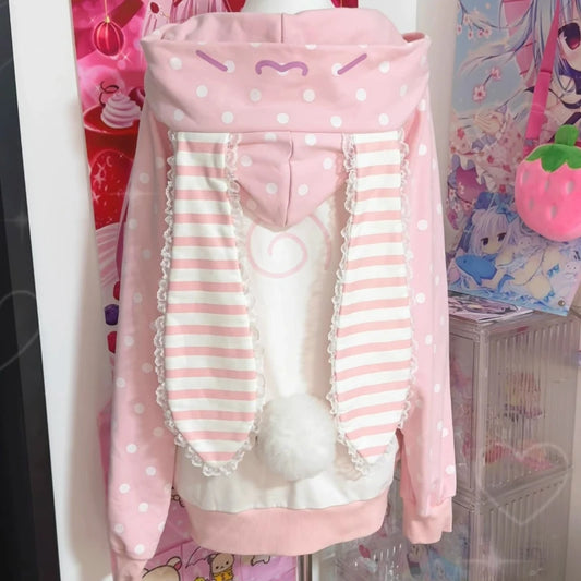 Pink and white polka dot hoodie with striped sleeves on a mannequin against a colorful background.
