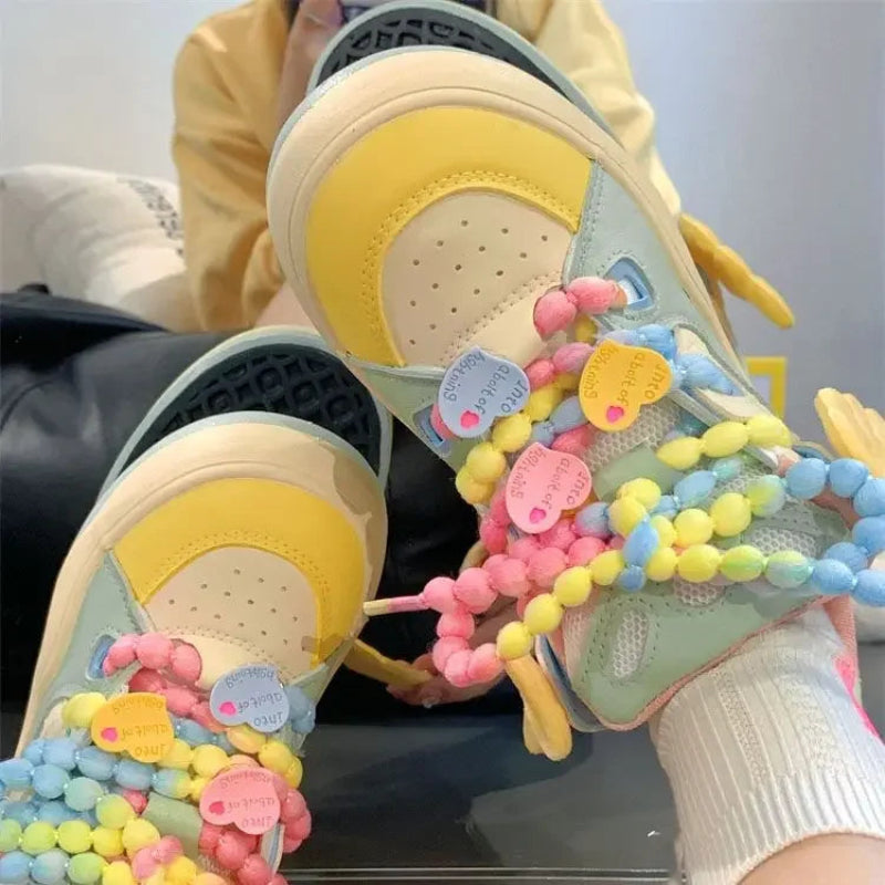 Angel on a rainbow platform sneakers, being displayed in front of a yellow hoodie and white wall.