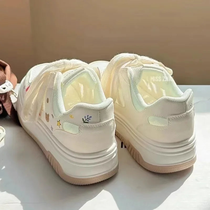 Pair of white sneakers with decorative elements on a light surface