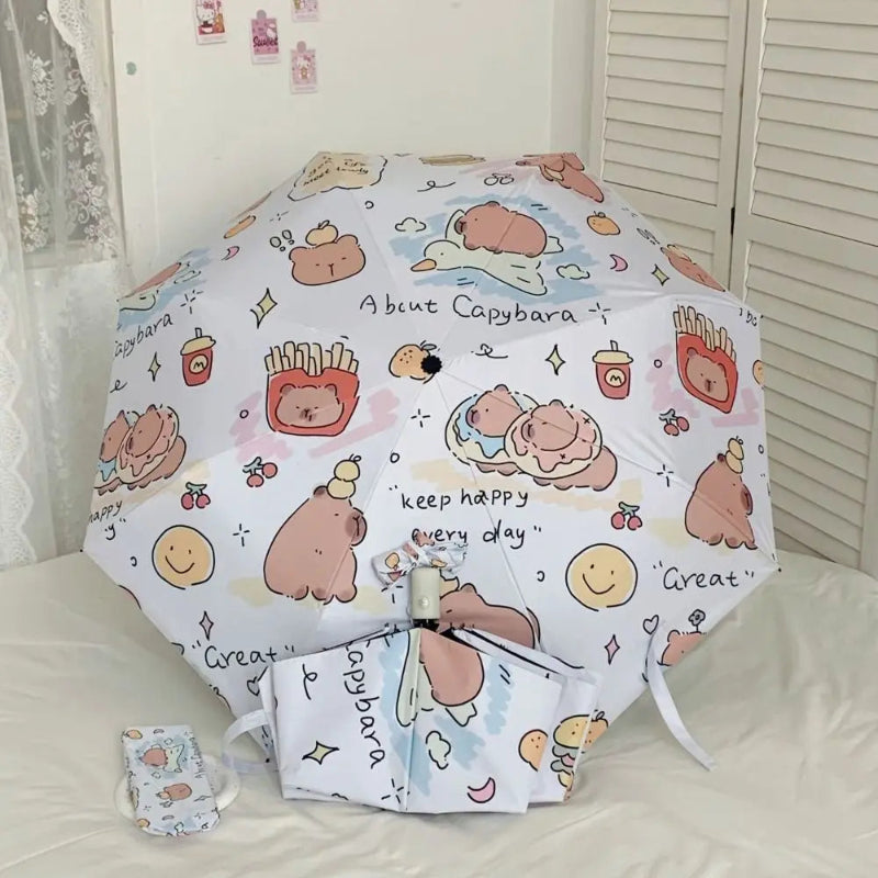 kawaii capybara umbrella displayed open along side a closed umbrella and a case for it on a beige background