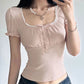 Woman wearing a pink top with lacey trim and dark jeans indoors.
