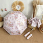 Pink umbrella with cartoon cat designs on a beige surface, surrounded by decorative items.