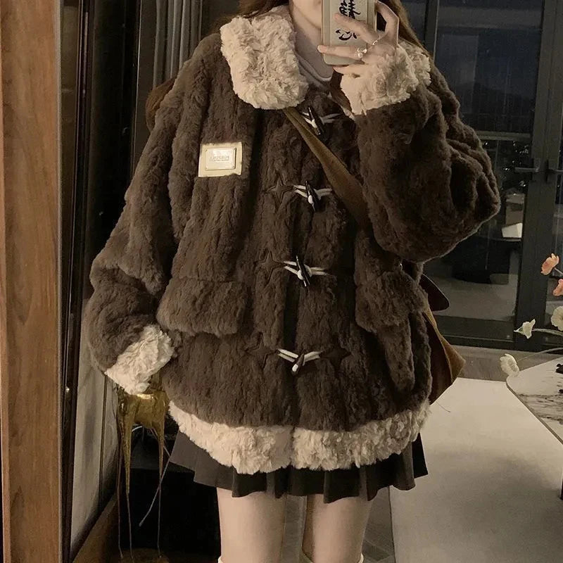 A person wearing an oversized dark brown faux-fur jacket with cream-colored faux-fur trim on the collar, cuffs, and hem, styled with a pleated dark skirt and a brown shoulder bag.