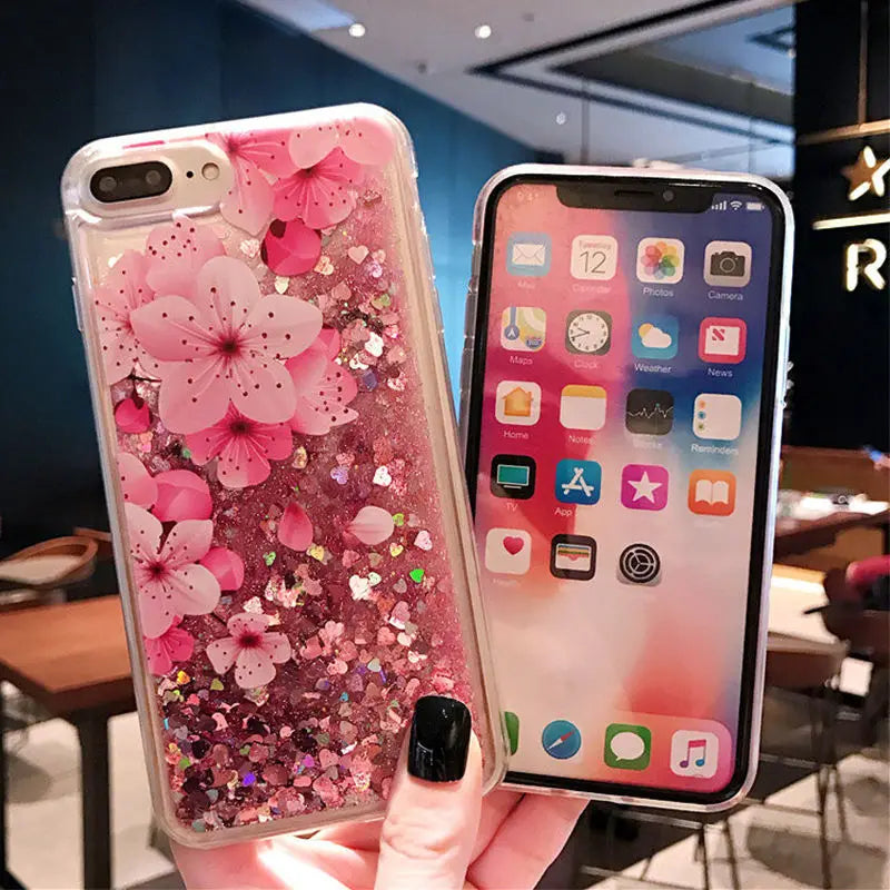 Phone case with pink cherry blossoms and glitter held by a hand in a restaurant setting