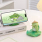 Phone with frog-themed phone holder and figurine on a desk