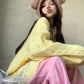 Person wearing a yellow sweater and pink skirt with a bear hat, sitting against a plain background.