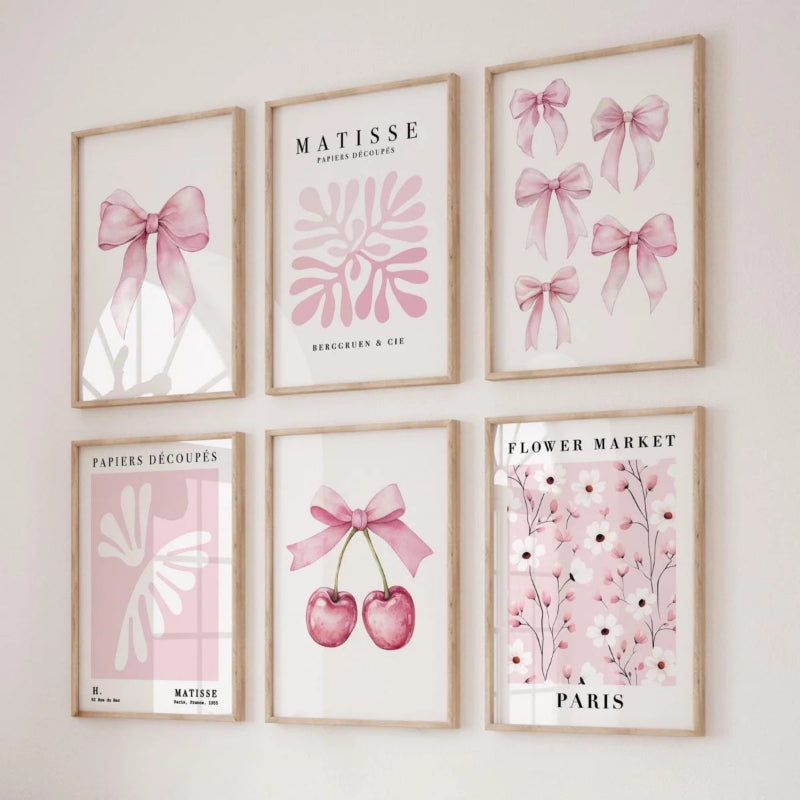 Six framed art prints arranged in a 2x3 grid on a light wall. The prints feature pink watercolor motifs including bows, cherry blossoms, flowers, and abstract shapes, with some prints displaying the text 'MATISSE', 'PARIS', and 'PARISERS DÉCOUPES'.