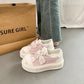 cute cat Pink and white sneakers with cartoon designs on a gray floor next to a paper bag.