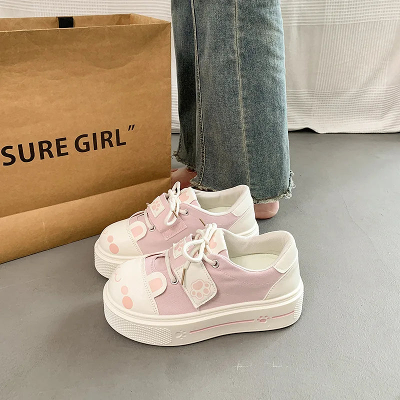 cute cat Pink and white sneakers with cartoon designs on a gray floor next to a paper bag.