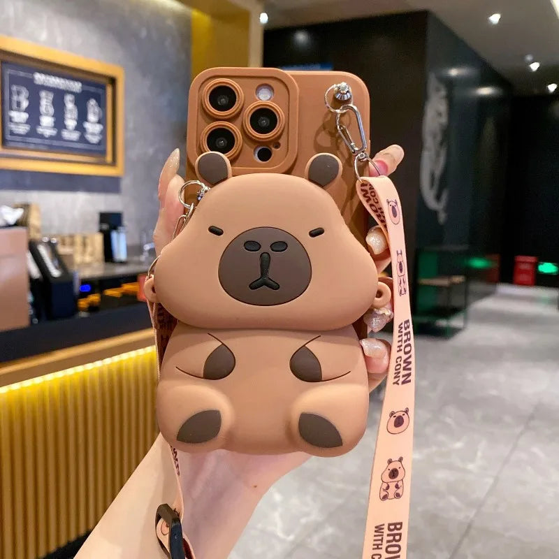 Dark Brown Capybara shaped phone case with a strap held in front of a blurred cafe background