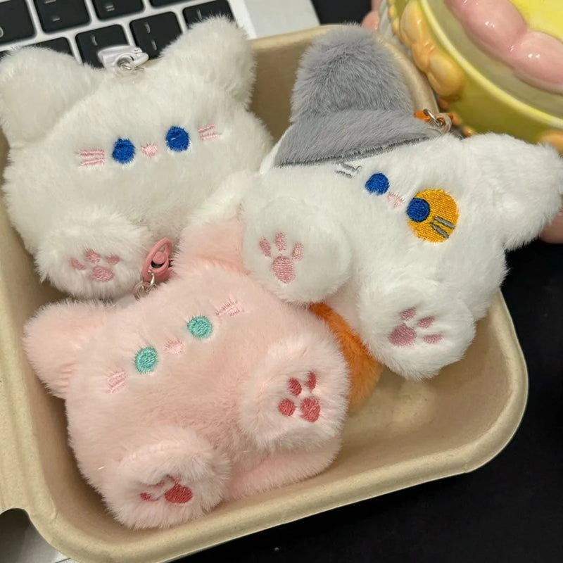 Three plush cat toys in a cardboard box with a laptop in the background