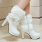 White high-heeled boots with fluffy fur and a bow on a neutral background