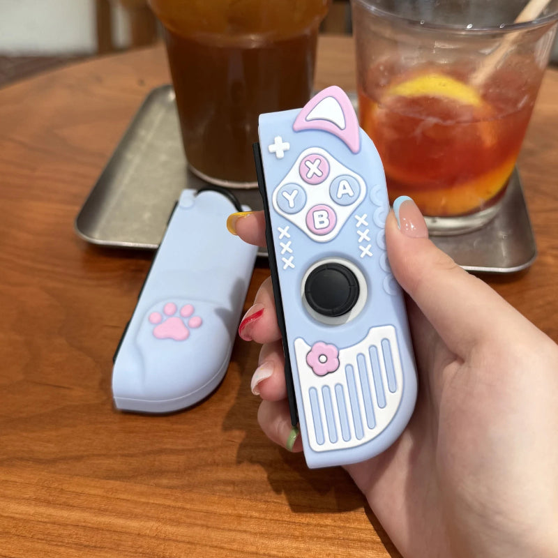 Hand holding a Nintendo Switch controller with kawaii design on a wooden table with drinks in the background