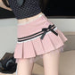 Person wearing a pink pleated skirt with a black ribbon on a neutral background