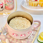 Pink ramen bowl with instant noodles on a table with fruit and drinks.