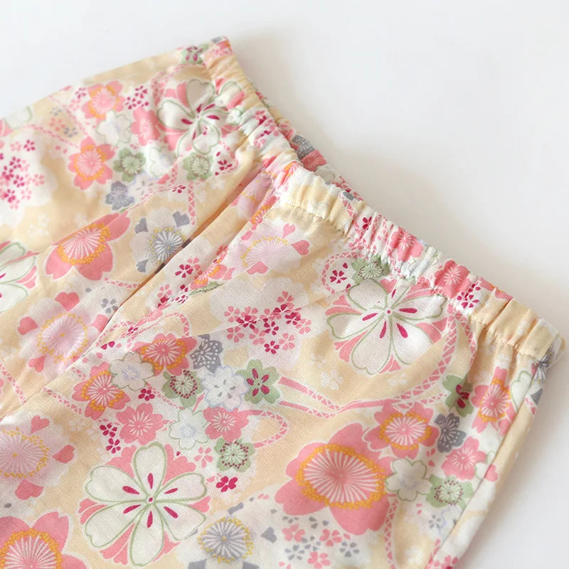 A close-up of a pair of children's shorts featuring a soft, pastel floral pattern on a pale yellow background. The shorts have an elastic waistband and are photographed on a clean, solid white background.