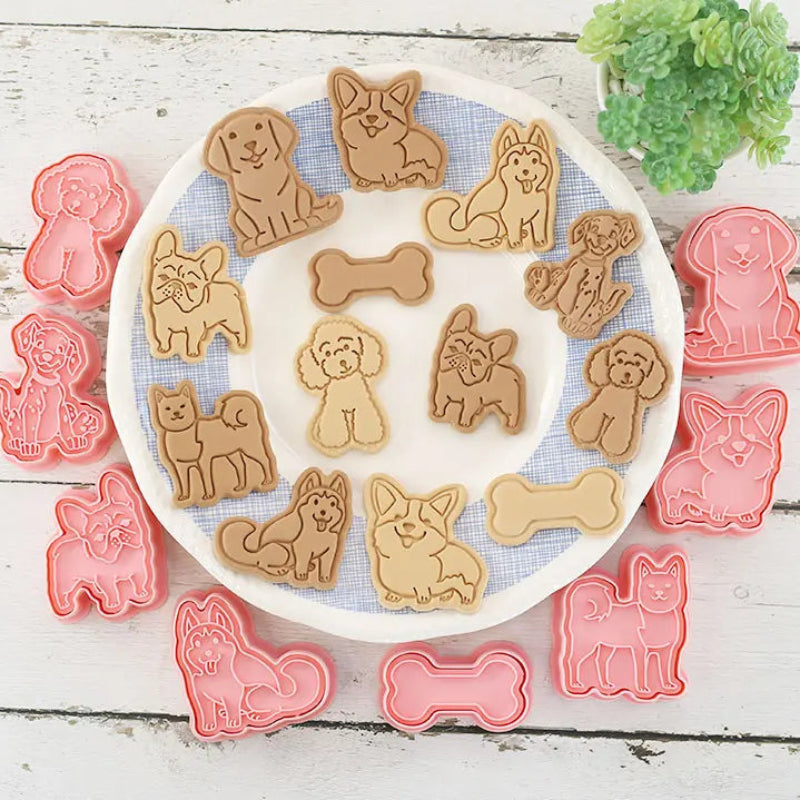 Dog-shaped cookie cutters on a white plate with cookies shaped like dogs and bones, surrounded by additional cutters on a wooden surface.