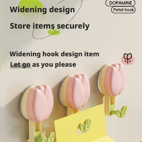 Three pink tulip-shaped wall hooks mounted on a wall, with a yellow paper towel holder in front. The image includes promotional text such as 'Widening design', 'Store items securely', and 'Let go as you please'.