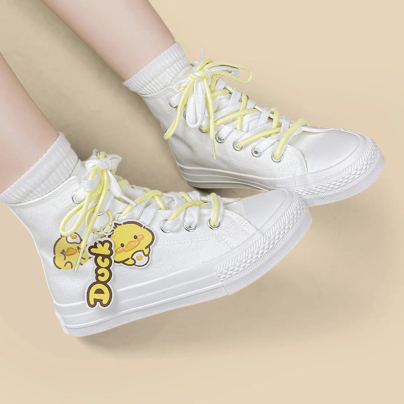 White high-top canvas sneakers with yellow laces and a yellow duck character charm, shown on a model's feet against a light beige background.