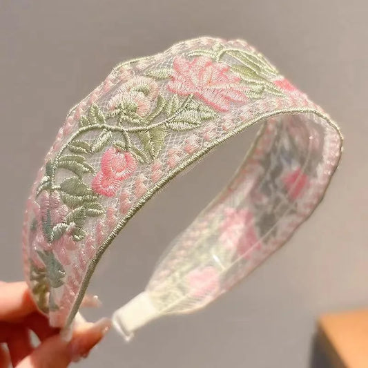 Embroidered cottagecore headband with floral design held by a hand against a neutral background