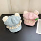 Two bear hats, one blue and one pink, with lace details on a dark surface.