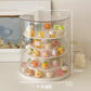 A clear cylindrical rotating display stand with white tiers holding many small pastel novelty items, shown on a tabletop with overlaid dimension labels (21.5 cm, 25.