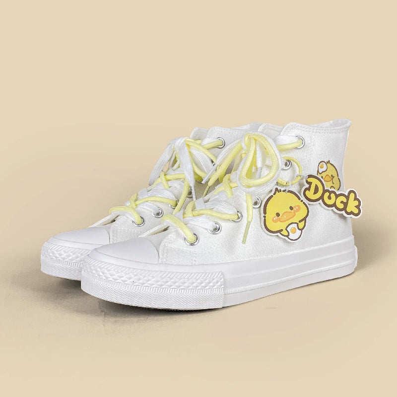 A pair of white high-top canvas sneakers with pale yellow laces and a yellow duck character patch on the side, set against a solid beige background.