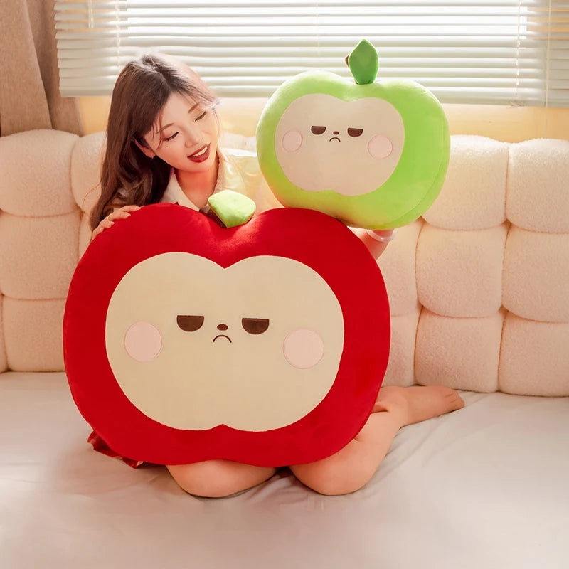Woman sitting on a couch with two large apple-shaped cushions, one red and one green.