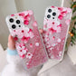 Two phone cases with pink cherry blossom design held by a person.